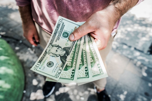 Osoba v bordovom tričku drží v ruke papierové peniaze.jpg