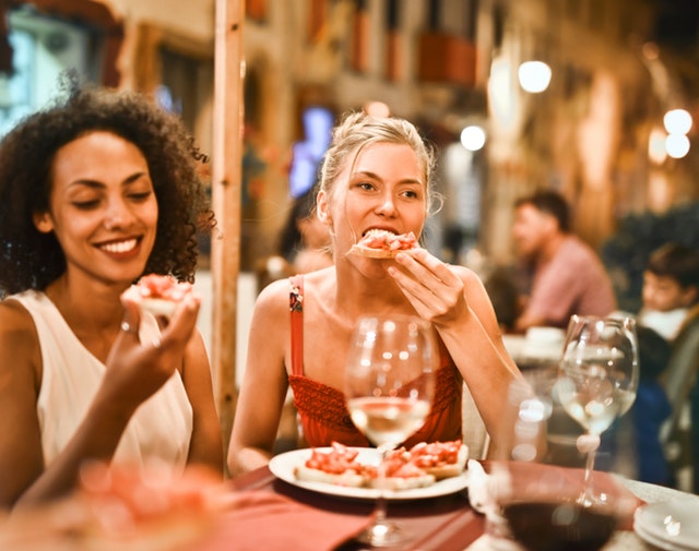 Ženy, ktoré jedia pizzu a na stole majú poháre s vínom.jpg